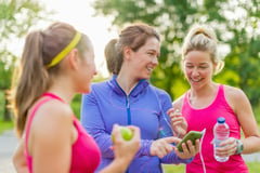 Group of happy active girls preparing for a run in nature by choosing music on a smart phone