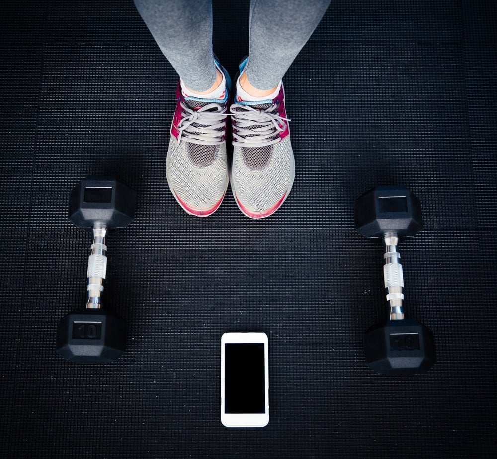 Closeup image of a female legs with dumbbells and smartphone on the floor at gym.jpeg