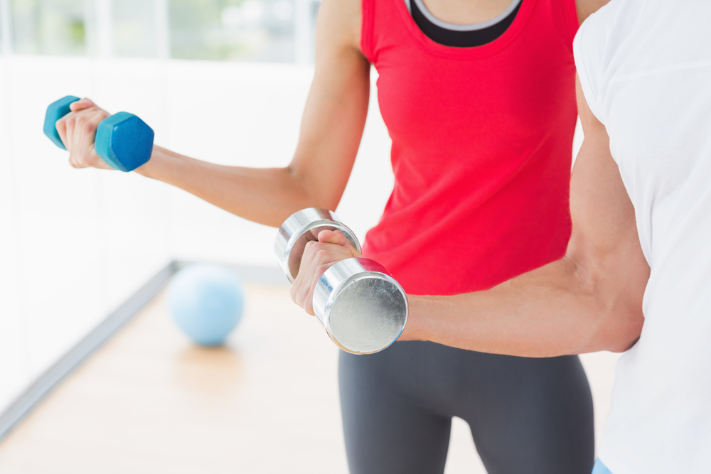 Close-up mid section of a sporty young couple with dumbbells in the gym